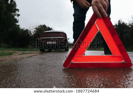 unrecognizable person placing an emergency red triangle on the road on a bad weather day. damaged car.