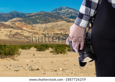 Professional photographer or hobbyist traveling through a desert landscape and holding a camera.  The view is a close up of the equipment so depict photography as an outdoor activity