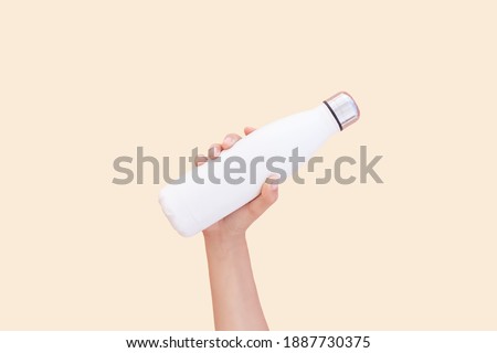 Close-up of hand holding white reusable steel thermo water bottle isolated on background of set sail champagne color, 2021 trend; with copy space. Royalty-Free Stock Photo #1887730375