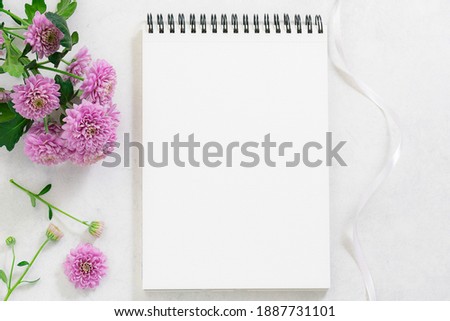Creative composition with blank notepad and beautiful aromatic flowers on white marble background. Mother’s Day. Birthday. St. Valentine’s Day greeting card template.