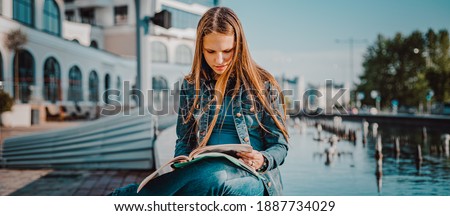 Back to school student teenager girl reads a textbook. Outdoor portrait of young teenager brunette girl with long hair. girl on city