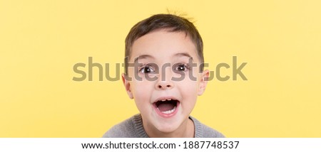 Emotional portrait of a child on a yellow background. The enthusiastic face is close. Eye contact. Vision, bright idea, advertising concept. Studio light. Trendy combination of gray and yellow in 2021
