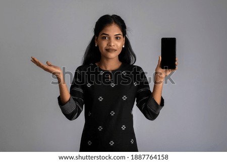 Young beautiful woman holding and showing blank screen of smartphone or mobile or tablet phone on a gray background.