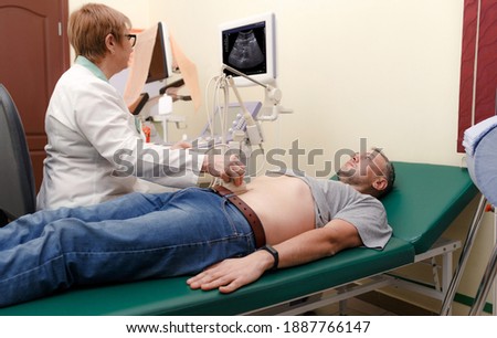 Ultrasound diagnosis of the stomach on the abdominal cavity of a man in the clinic, close-up. The doctor runs an ultrasound sensor over the patient's male abdomen and looks at the image on the screen. Royalty-Free Stock Photo #1887766147