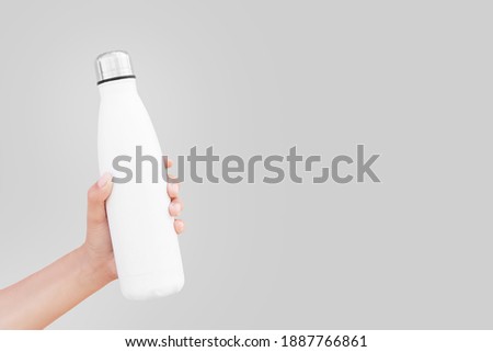 Close-up of hand holding white reusable steel thermo water bottle isolated on background of ultimate gray color, 2021 trend; with copy space.