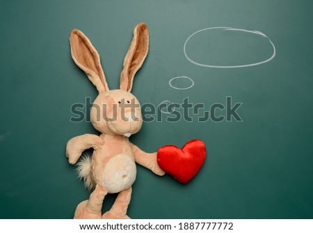 cute teddy bunny holding a textile red heart on a green background, love and dreams concept