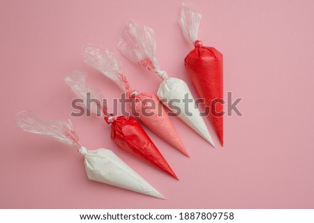 Multicolored glazing in icing bags on a pink background. Set for decorating desserts.  
Icing for gingerbread, brownies and cakes in pastry bags. Cake decorating tools.