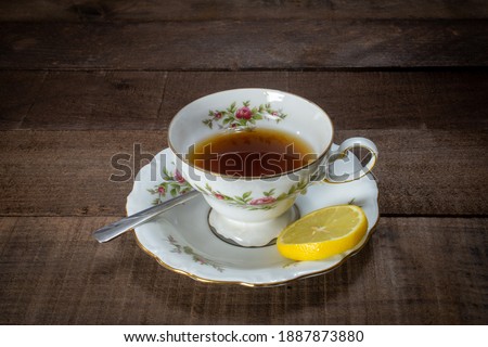 Tea filled teacup with lemon and silver spoon on dark wood.