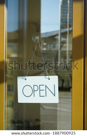 Close up of white  open sign hanging on glass door of cafe. Blurry background. Opened concept. 