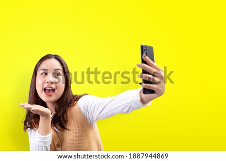 Happy pretty girl makes self-portrait on the smartphone over yellow background.