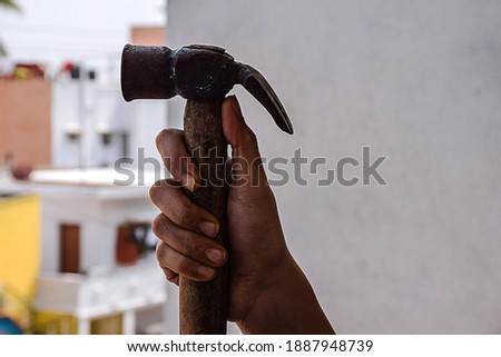 A man holding a iron hammer with wooden handel in his right hand.