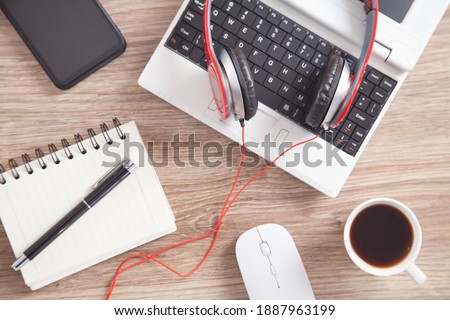 Red headphones, coffee, computer keyboard and other objects on the wooden desk.