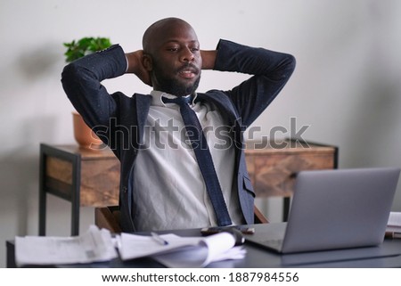 Relaxed worker finished work completed task taking break after hard workday putting head on hand. Thoughtful African American businessman looking out window sitting at office desk. Royalty-Free Stock Photo #1887984556