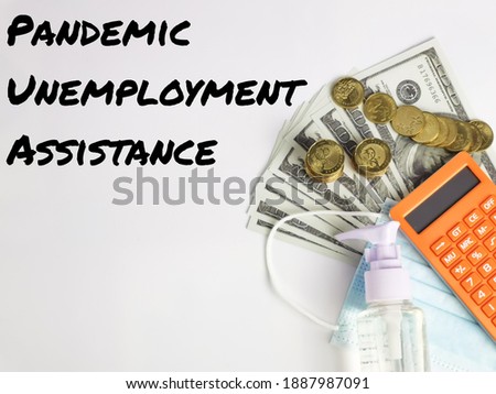 Pandemic Unemployment Assistance written on white background with calculator,hand sanitizer,face mask,fake money and coins.Business and finance concept.