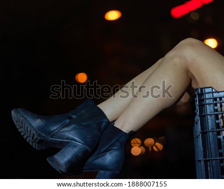 The crossed legs of a woman wearing black boots dangle over the edge of a milk crate.