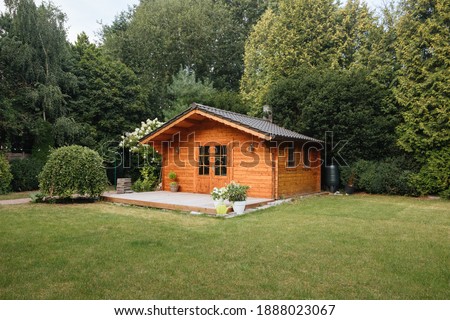 Orange wooden hut in the garden with many tall trees. Garden shed with lawn in front of him Royalty-Free Stock Photo #1888023067