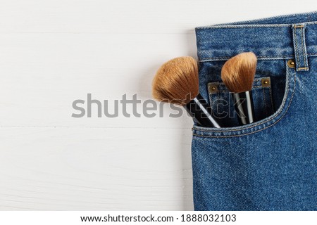 Large makeup brushes in pocket of blue jeans. Concept, commercial work of a makeup artist, for printing business cards and brochures.