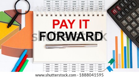 Notepad with text PAY IT FORWARD on business charts and pen