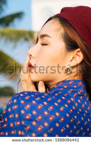 Close up shot of wavy brunette woman in blue and red retro dress touch her mouth in sunlight, vertical.