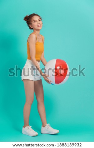Young beautiful Asian woman with beach accessories holding colorful ball in bright background.