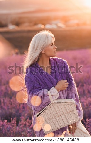 Beautiful blonde woman resting in lavender field holding straw basket over sunset nature background close up. Summr season. Vacation time. 20s. 