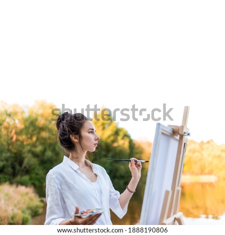White background free for text, woman draws picture of landscape, in summer pond of lake, white shirt, creating a creative artistic mood. Brush and color palette with paints