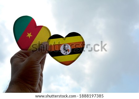 Hand holds a heart Shape Cameroon and Uganda flag, love between two countries
