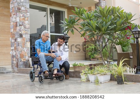 Sick Old man in a Wheelchair is Receiving a Help From a Young Doctor in Home Visit. 