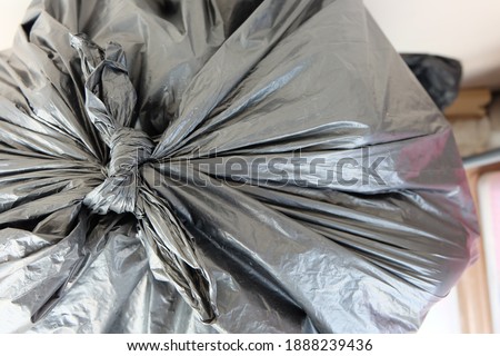 Tall, white trash bin with built-in trash on the floor.A large black garbage bag tied into the mouth of the sealed bag.