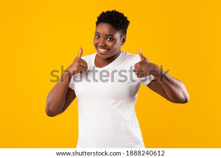Cheerful Overweight African American Woman Gesturing Thumbs-Up With Both Hands Approving And Advertising Something Standing On Yellow Background, Studio Shot. Thumbs-Up, Like Gesture
