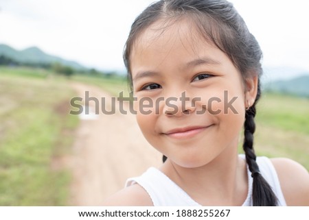 Beautiful asian little girl on the meadow in summer day. Happy little girl in a hat on a background of nature. Happy childhood concept.