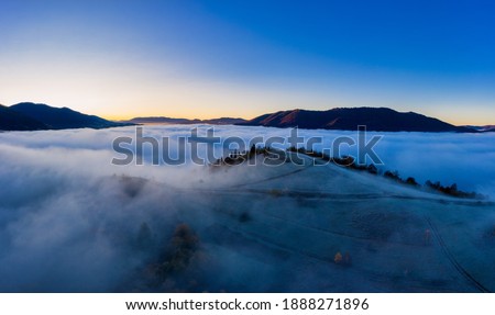 Sunrise over mountain hils covered with gray mist. Aerial panoramic drone shot