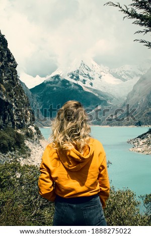 Girl with yellow cap and brown backpack looking at Turquoise lake in the andes mountains in peru. Laguna Paron