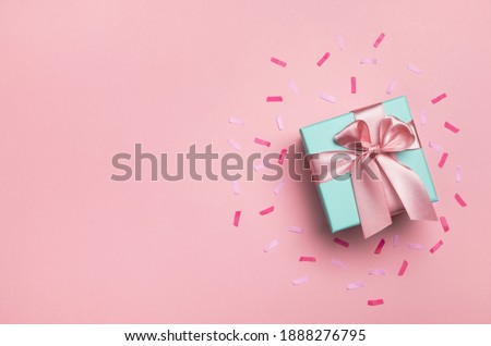 Gift box and confetti on pastel pink background. Birthday party, Valentines day or mother day greeting card. Top view, flat lay, copy space