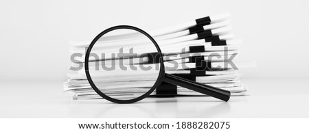 Stack of report paper documents with magnifying glass. Concept of business and search.