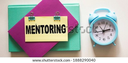 Alarm clock and notepads with the inscription Mentoring on a white background