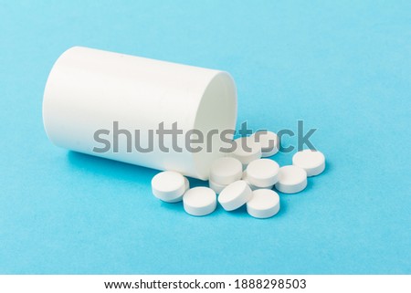 Medication bottle and white pills spilled on blue pastel coloured background. Medication and prescription pills.