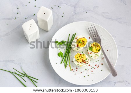 Boiled Eggs on a White Dish Garnished with Black Pepper, Chili Flakes, Salt and Chives Directly Above  Photo