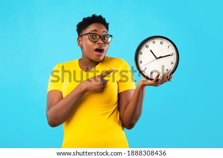 Deadline, Time Is Over. Oversized African Woman Showing Clock Posing Standing Over Blue Studio Background, Looking At Camera. Shocked Black Lady Being Late. Time's Tickling Concept Royalty-Free Stock Photo #1888308436