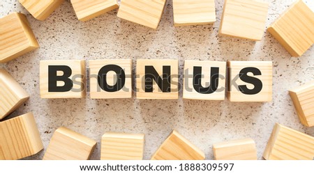 The word BONUS consists of wooden cubes with letters, top view on a light background. Work space.