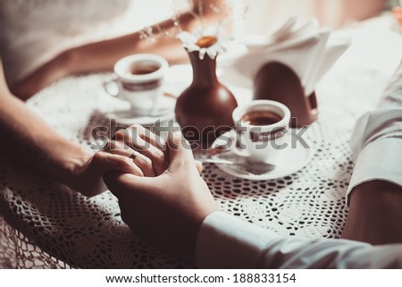 Couple in love drink coffee in cafe, holding each other's hand. Photo is processed in coffee color tone. Concept of male and female hands, love and coffee. Focused on hands.