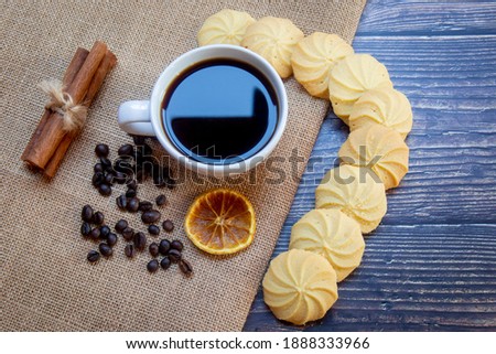 Black coffee, cookies are placed on a wooden table and a light brown cloth.