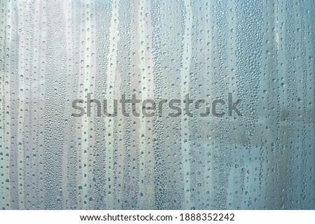 Wet glass with large drops of water or rain of blue color. Background or wallpaper with water texture close-up. Image of water droplets on a clear glass surface during heavy rain