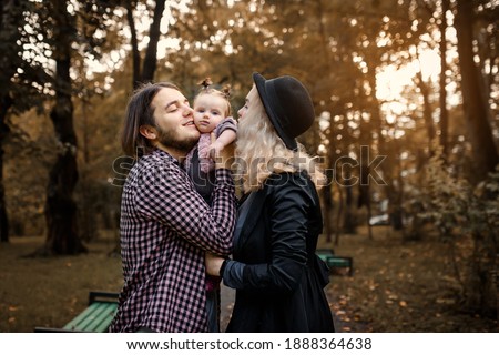 Happy young family concept. Young father and mother are kissing their 6 month old baby child girl in the park during the fall walk. 