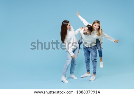 Full length of smiling young parents mom dad with child kid daughter teen girl in sweaters giving piggyback ride to joyful, sitting on back isolated on blue background. Family day parenthood concept