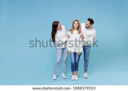 Full length of cheerful young happy parents mom dad with child kid daughter teen girl in casual white sweaters hugging isolated on blue color background studio portrait. Family day parenthood concept