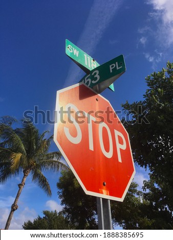 Red stop sign warning safety directions in public Miami Dade neighborhood community in Florida on a hot sunny day with tropical palm trees and bright blue sky