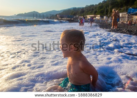 a child sits on the seashore and laughs