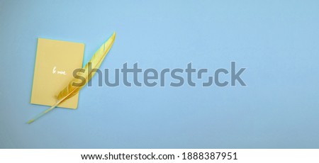 Valentine's day simple composition background with yellow notebook and stylish colored feather on pastel banner, copy space photo