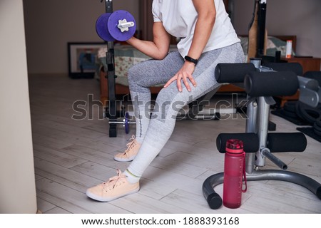 Cropped photo of a Caucasian female bodybuilder doing the seated bicep curl on the bench